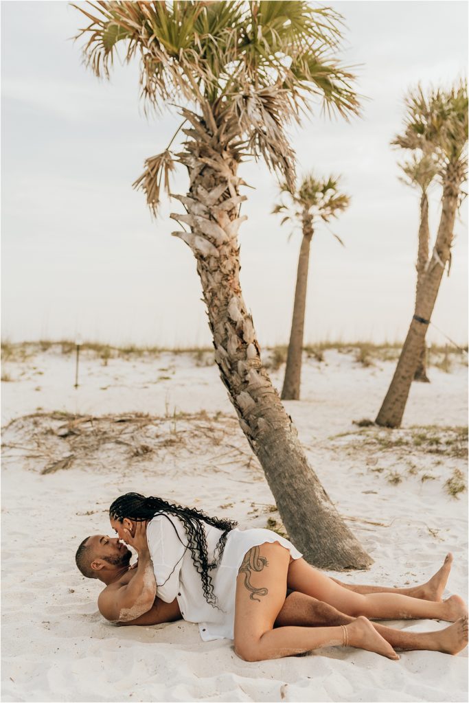 black couple on beach rolling in sand under palm tree
