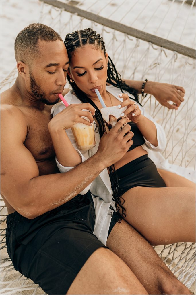 black couple sharing drinks in hammock on beach