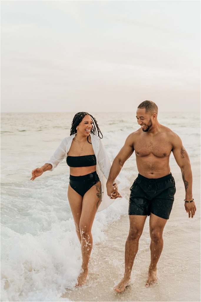 couple running and kicking water on beach engagement session
