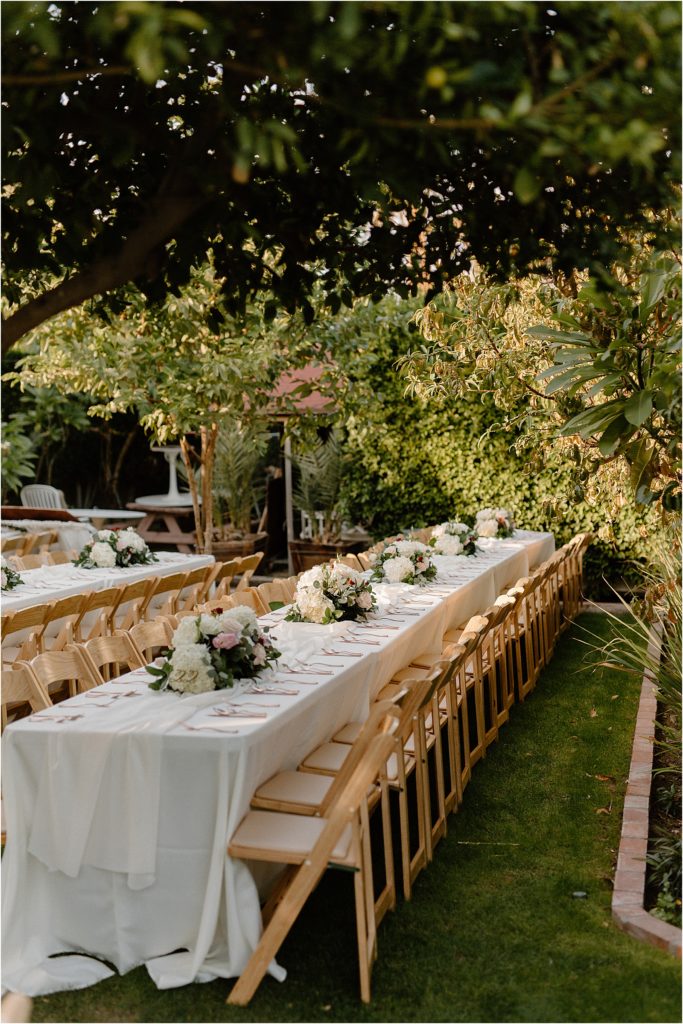 rows of tables with natural wood chairs and floral arrangements in garden at backyard palm springs wedding venue